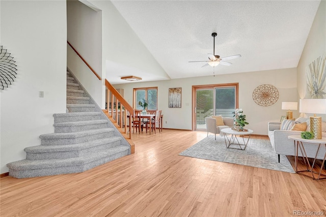 living room with lofted ceiling, light wood-type flooring, ceiling fan, and a textured ceiling