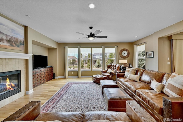 living room with ceiling fan, a tile fireplace, light hardwood / wood-style floors, and a textured ceiling