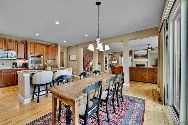 dining room with ceiling fan with notable chandelier and light wood-type flooring