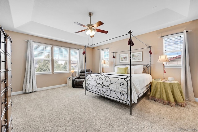 carpeted bedroom with multiple windows, a raised ceiling, and ceiling fan