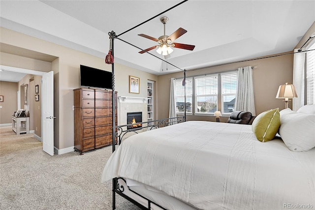 carpeted bedroom featuring a tiled fireplace, ceiling fan, and a tray ceiling