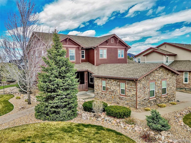 craftsman inspired home featuring stone siding, a shingled roof, fence, and covered porch