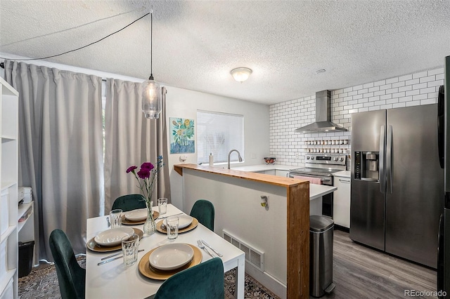 kitchen with wall chimney exhaust hood, decorative light fixtures, kitchen peninsula, stainless steel appliances, and backsplash