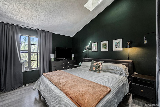 bedroom featuring wood-type flooring, vaulted ceiling with skylight, and a textured ceiling