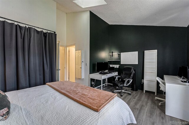 bedroom with hardwood / wood-style floors, a skylight, high vaulted ceiling, and a textured ceiling