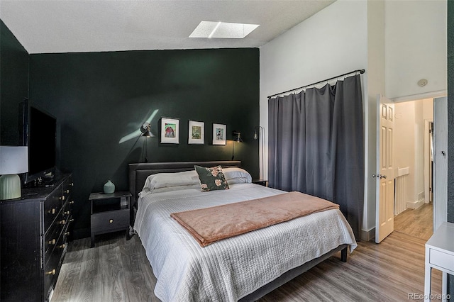 bedroom with wood-type flooring, a skylight, and high vaulted ceiling