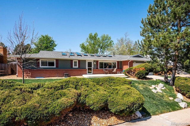 single story home featuring solar panels, brick siding, and a front lawn