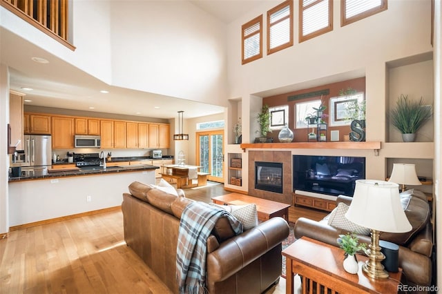 living room featuring a fireplace, a high ceiling, light hardwood / wood-style floors, and sink