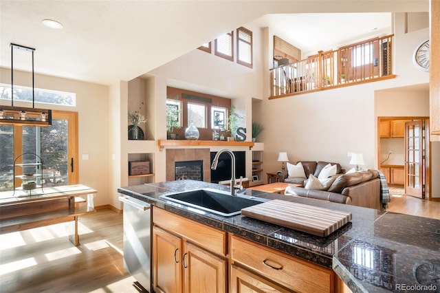 kitchen with dishwasher, sink, a high ceiling, pendant lighting, and light wood-type flooring