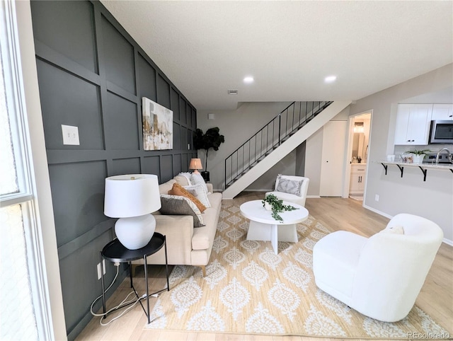 living area with recessed lighting, light wood-style flooring, stairs, and a decorative wall