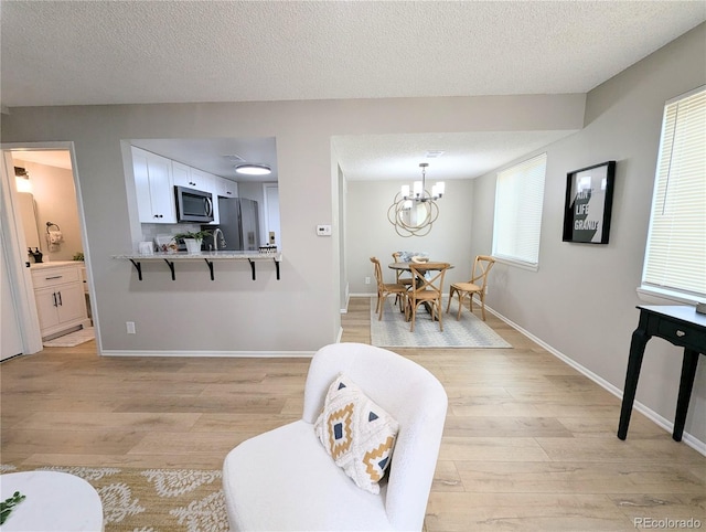 living area with baseboards, a textured ceiling, a chandelier, and light wood finished floors