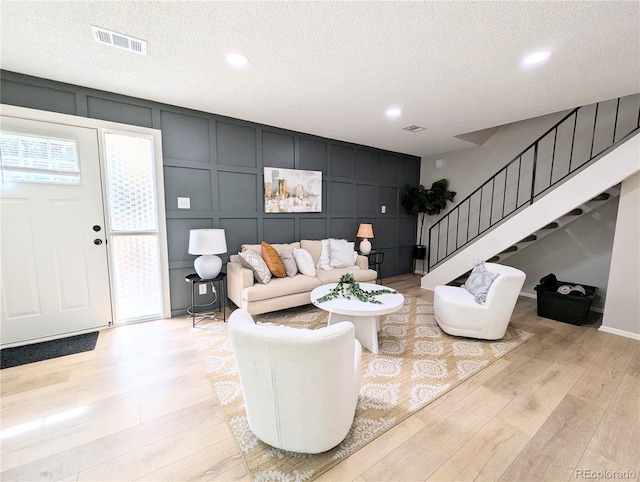 living room featuring visible vents, stairs, a textured ceiling, a decorative wall, and light wood-type flooring