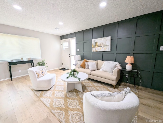 living area featuring baseboards, light wood finished floors, a textured ceiling, and a decorative wall