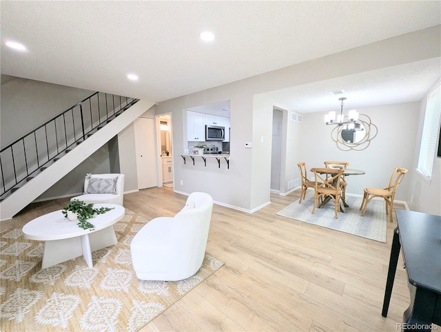 living room with visible vents, baseboards, light wood finished floors, an inviting chandelier, and stairs