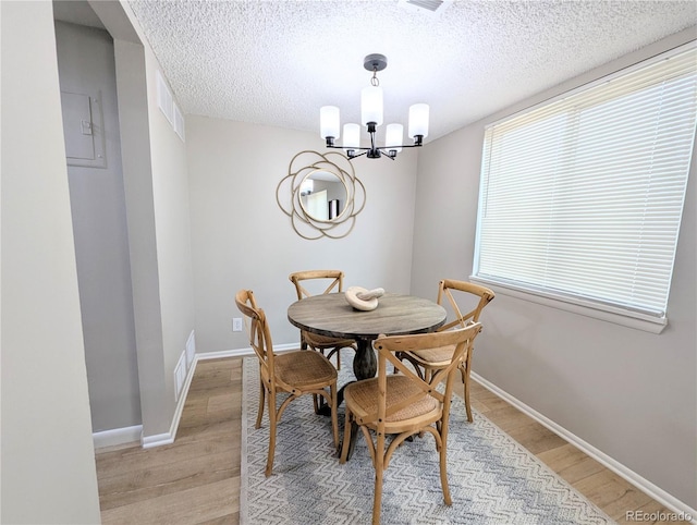 dining room featuring light wood-type flooring, baseboards, a textured ceiling, and an inviting chandelier