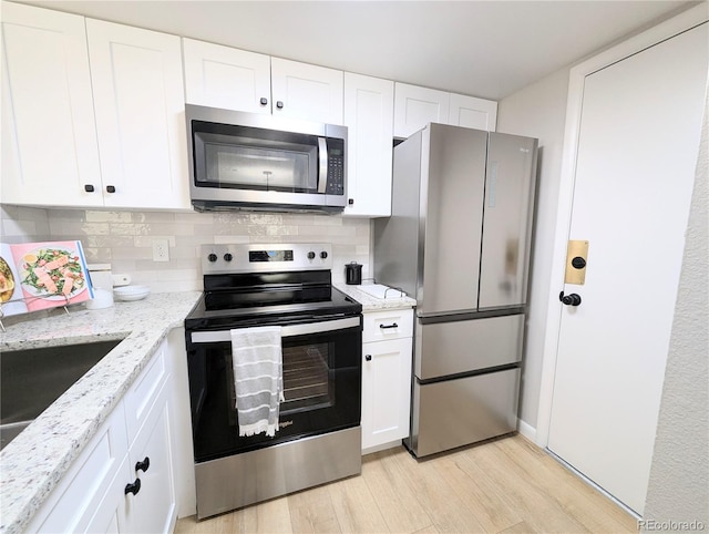 kitchen with backsplash, light stone counters, appliances with stainless steel finishes, light wood-style floors, and white cabinetry