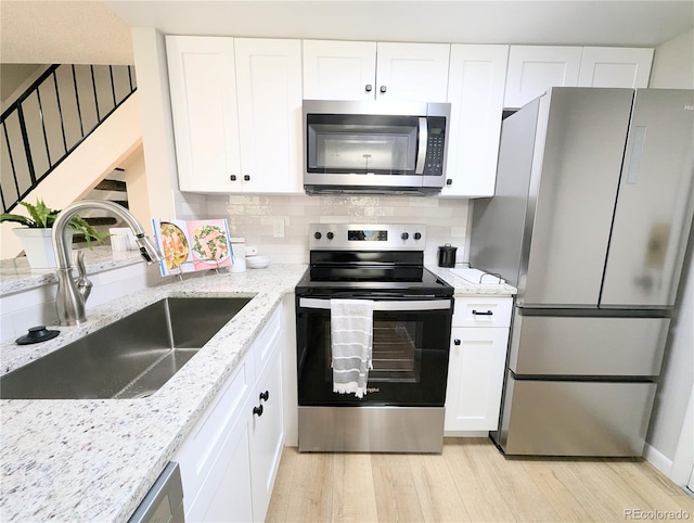 kitchen featuring light wood-style flooring, a sink, appliances with stainless steel finishes, white cabinets, and decorative backsplash