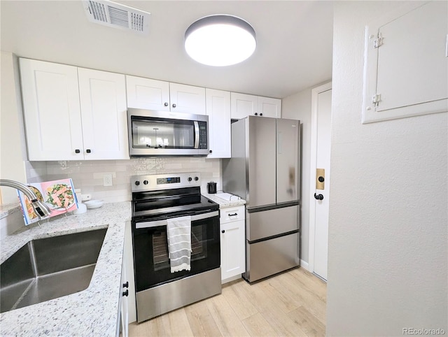 kitchen with light wood finished floors, visible vents, decorative backsplash, stainless steel appliances, and a sink