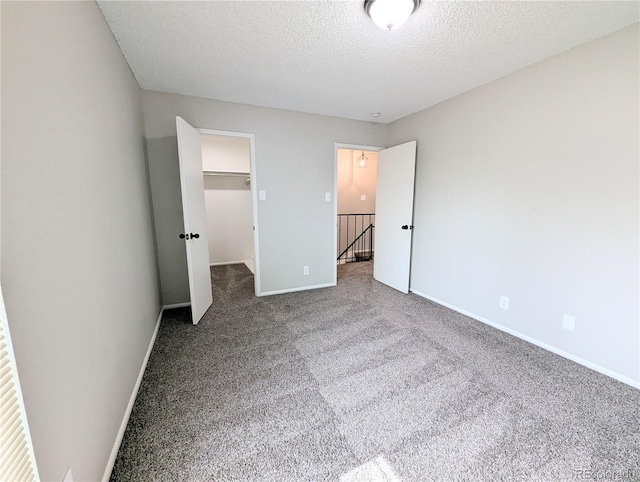 unfurnished bedroom with a walk in closet, baseboards, carpet floors, a closet, and a textured ceiling