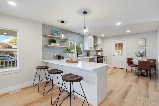 kitchen featuring decorative light fixtures, wall chimney range hood, kitchen peninsula, a kitchen bar, and white cabinets