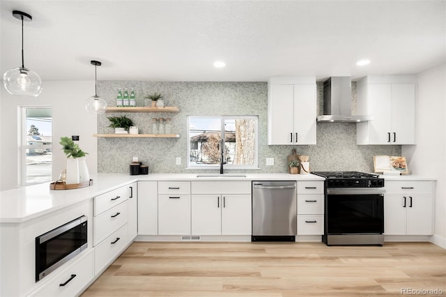 kitchen featuring decorative light fixtures, wall chimney range hood, white cabinetry, stainless steel appliances, and sink