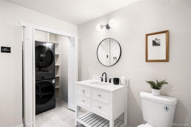 bathroom with stacked washer / drying machine, vanity, toilet, and hardwood / wood-style floors