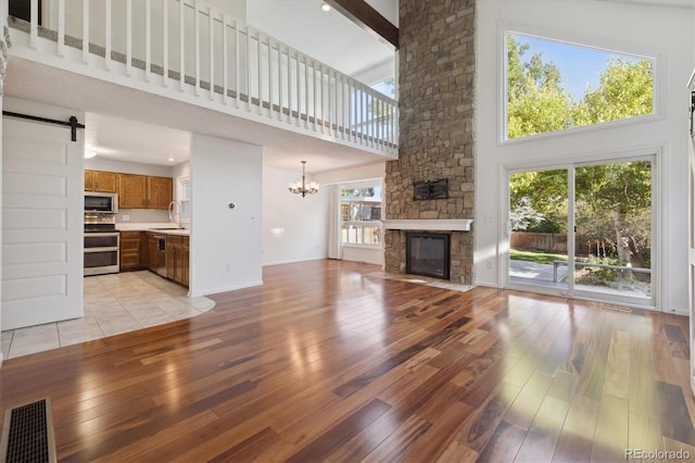 unfurnished living room featuring a barn door, light hardwood / wood-style flooring, high vaulted ceiling, and a healthy amount of sunlight