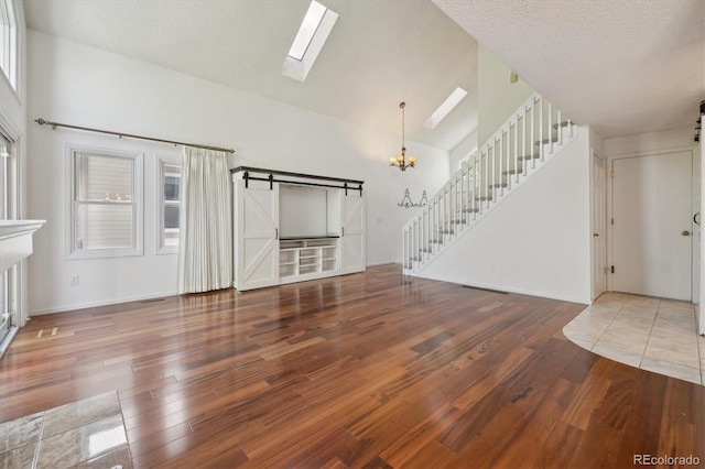 unfurnished living room featuring hardwood / wood-style flooring, plenty of natural light, a barn door, and high vaulted ceiling