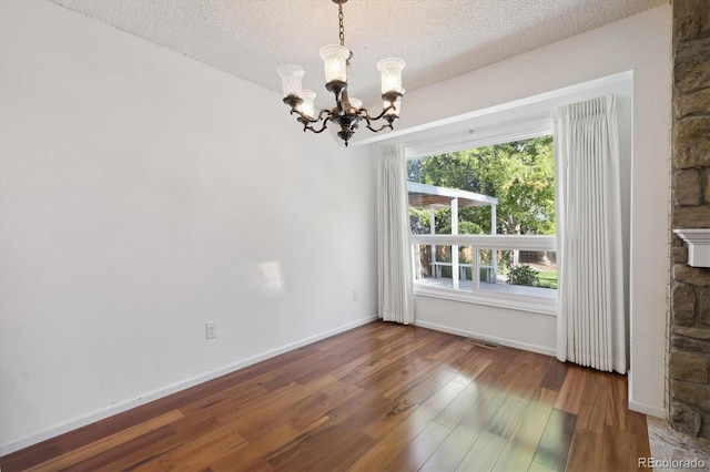 unfurnished dining area featuring wood-type flooring, a textured ceiling, and a notable chandelier