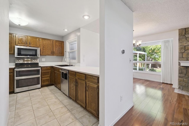 kitchen with appliances with stainless steel finishes, light wood-type flooring, sink, pendant lighting, and an inviting chandelier