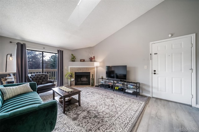 living room with a textured ceiling, hardwood / wood-style floors, lofted ceiling with skylight, and a tiled fireplace