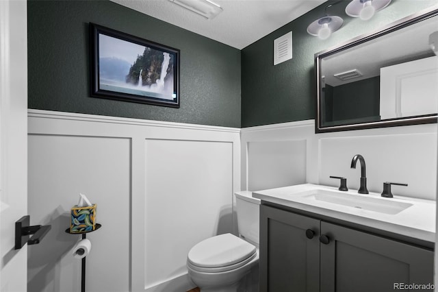 1113 Southbury Pl, Highlands Ranch, CO 80129 - bathroom featuring a textured wall, toilet, a wainscoted wall, vanity, and a decorative wall