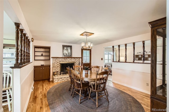 dining room with a fireplace, light wood-style floors, a chandelier, and baseboards