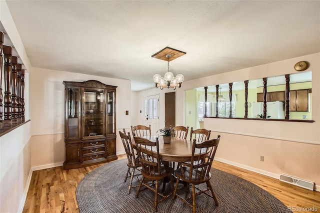 dining space featuring baseboards, light wood-style flooring, visible vents, and a notable chandelier