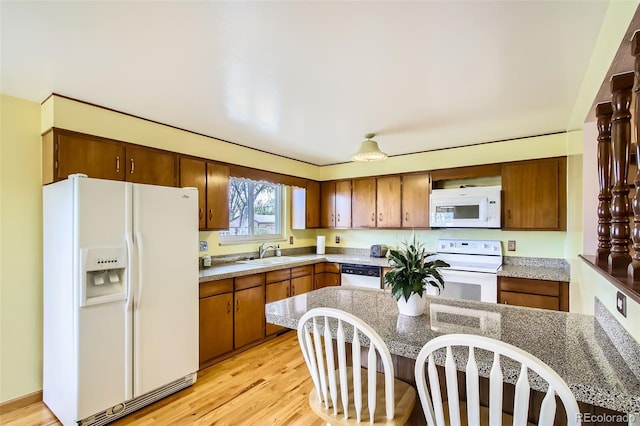 kitchen with a kitchen breakfast bar, a sink, light wood-style floors, white appliances, and brown cabinets