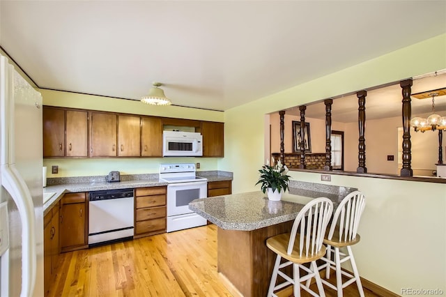 kitchen featuring brown cabinets, a breakfast bar, white appliances, light wood finished floors, and a peninsula