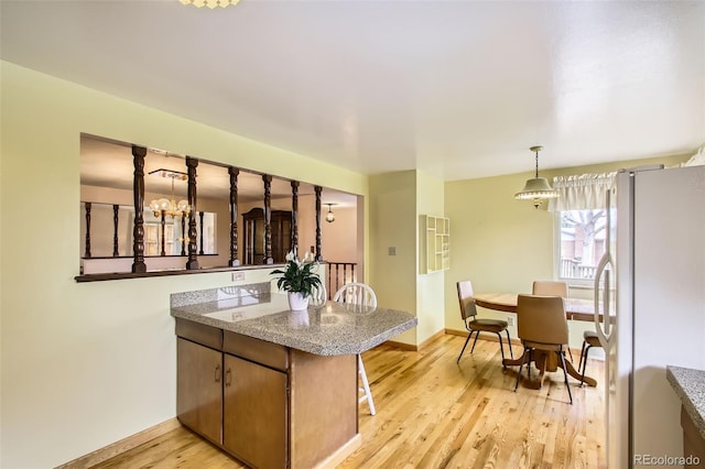 kitchen with an inviting chandelier, freestanding refrigerator, baseboards, a peninsula, and light wood-style flooring
