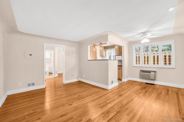 unfurnished living room featuring baseboards, visible vents, a wall unit AC, and light wood finished floors