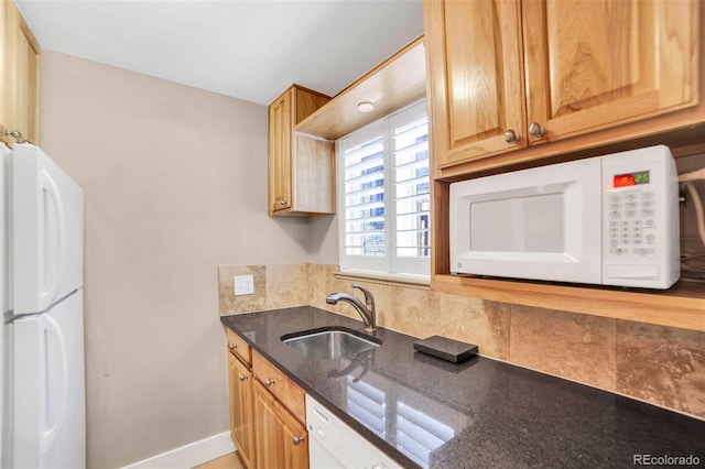 kitchen with white appliances, a sink, baseboards, decorative backsplash, and dark stone countertops