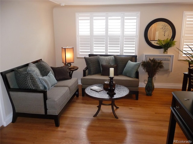 living room with a wall unit AC, light wood-style flooring, and baseboards