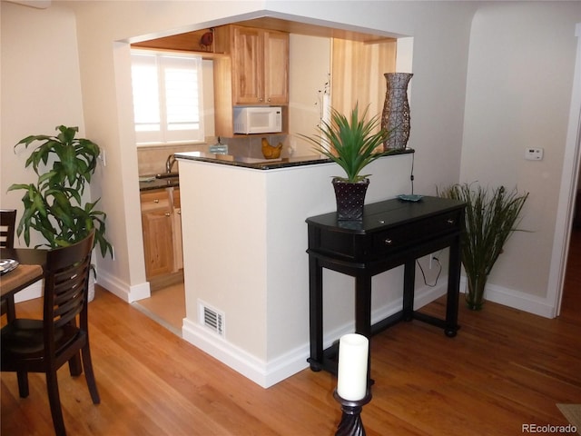 kitchen with dark countertops, white microwave, light wood-style flooring, and visible vents