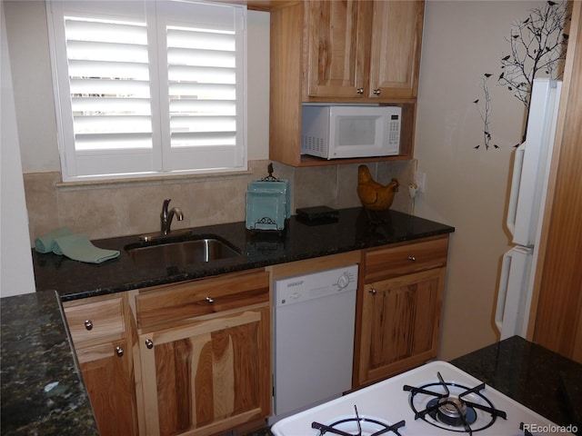 kitchen with decorative backsplash, brown cabinetry, a sink, dark stone counters, and white appliances