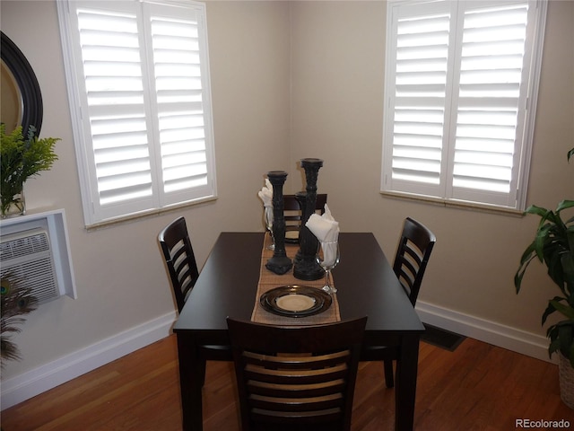 dining room featuring a wall unit AC, wood finished floors, and baseboards