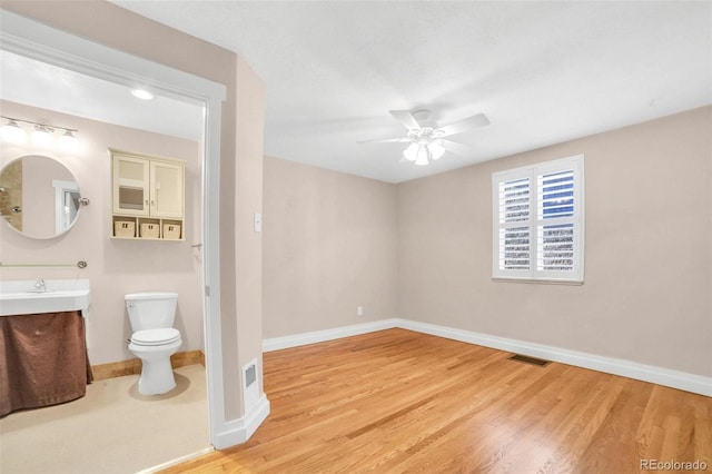 empty room featuring light wood finished floors, a ceiling fan, visible vents, and baseboards