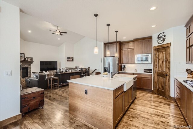 kitchen featuring open floor plan, stainless steel appliances, a stone fireplace, light wood-style floors, and a sink