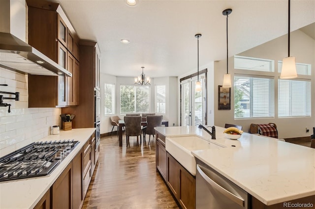 kitchen with glass insert cabinets, appliances with stainless steel finishes, wall chimney range hood, pendant lighting, and a sink