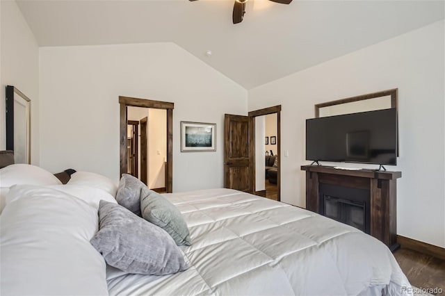 bedroom with a ceiling fan, a glass covered fireplace, vaulted ceiling, wood finished floors, and baseboards