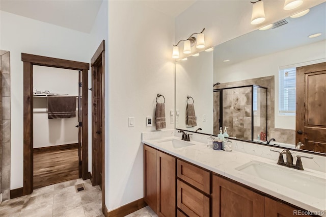 bathroom with double vanity, a shower stall, a spacious closet, and a sink