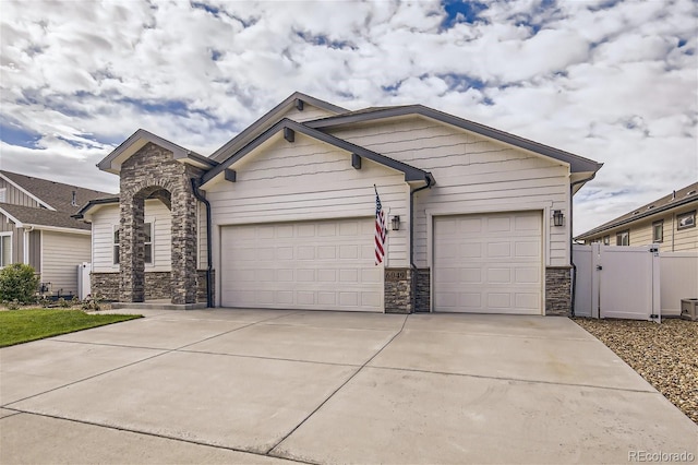 view of front facade featuring stone siding, driveway, an attached garage, and fence