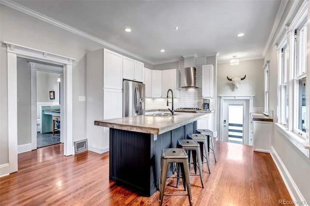 1399 Newton St, Denver, CO 80204 - kitchen with stainless steel fridge with ice dispenser, a breakfast bar, wood finished floors, white cabinets, and ornamental molding